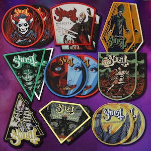 Könnte beinhalten: Eine Sammlung bestickter Stoffaufnäher mit verschiedenen Ghost-Band-Motiven, darunter kreisförmige, dreieckige, rautenförmige und sargförmige Designs. Die Aufnäher zeigen farbenfrohe grafische Illustrationen von Figuren, Totenköpfen und dem Ghost-Logo-Schriftzug.