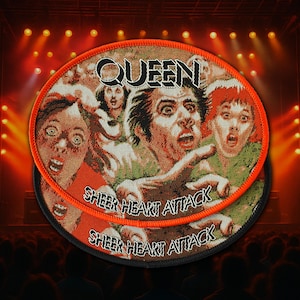 Puede incluir: Un parche tejido circular que presenta el logotipo de la banda Queen y el texto Sheer Heart Attack. El diseño muestra un collage de tres rostros expresivos con ojos muy abiertos y bocas abiertas, en tonos rojo, verde y blanco con un borde naranja.