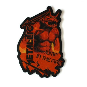 May include: A rectangular embroidered patch with a black border featuring a red and orange demon figure. The text METALLICA is vertically oriented on the left side, and the text JUMP IN THE FIRE is printed in black on the lower right section.