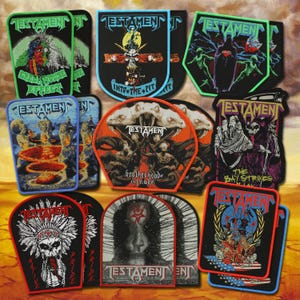 May include: A collection of embroidered fabric patches featuring the band Testament. Each patch displays unique graphic artwork, including skulls, figures, and band logos with text such as Green House Effect, Into the Pit, Brotherhood of the Snake, and The Bay Strikes Back.