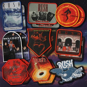 Puede incluir: Una colección de parches de la banda Rush en varias formas y diseños. Los parches presentan arte de álbumes, logotipos de bandas y texto como "Grace Under Pressure", "Spirit of Radio" y "Fly By Night". Los colores incluyen rojo, negro, azul y blanco.