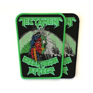 May include: A rectangular embroidered patch with a black background and a bright green border. It features the word TESTAMENT in green at the top, a central graphic of a face, and the words GREEN HOUSE EFFECT in green at the bottom.