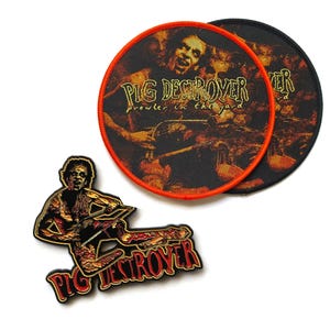 May include: Two circular fabric patches with orange and black borders featuring the Pig Destroyer Prowler in the Yard album art, alongside a die-cut metal enamel pin depicting a figure with a saw and the text Pig Destroyer in red.