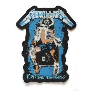 May include: A black fabric patch featuring the Metallica logo in white and blue at the top. The center graphic depicts a skeleton in blue shorts being electrocuted by lightning. The text RIDE THE LIGHTNING is printed in blue at the bottom.
