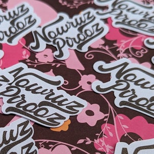 May include: A collection of white stickers with the text "Nowruz Pirooz" in brown lettering on a brown and pink floral background.
