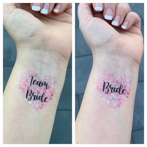 Könnte beinhalten: Zwei temporäre Tattoos, eines mit dem Text "Team Bride" und das andere mit dem Text "Bride". Beide Tattoos zeigen eine Herzform aus rosa Herzen.