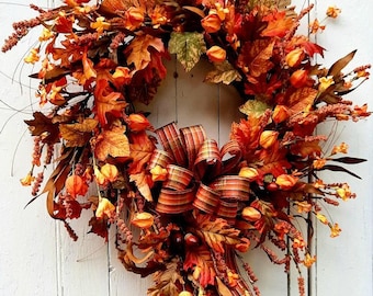 May include: A fall-themed wreath with a variety of autumn foliage, including leaves and berries in shades of orange, red, and brown. A large, striped bow adds a decorative touch. The wreath is displayed against a white background.
