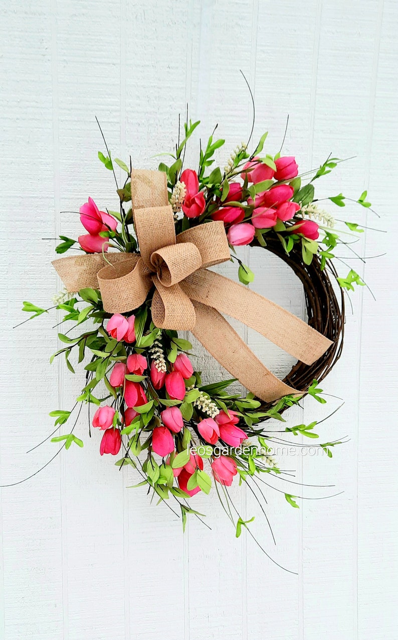 K&ouml;nnte beinhalten: Ein Kranz aus rosa Tulpen mit einer Schleife aus Sackleinen. Der Kranz ist aus Weinreben gefertigt und mit rosa Tulpen und Gr&uuml;n verziert.
