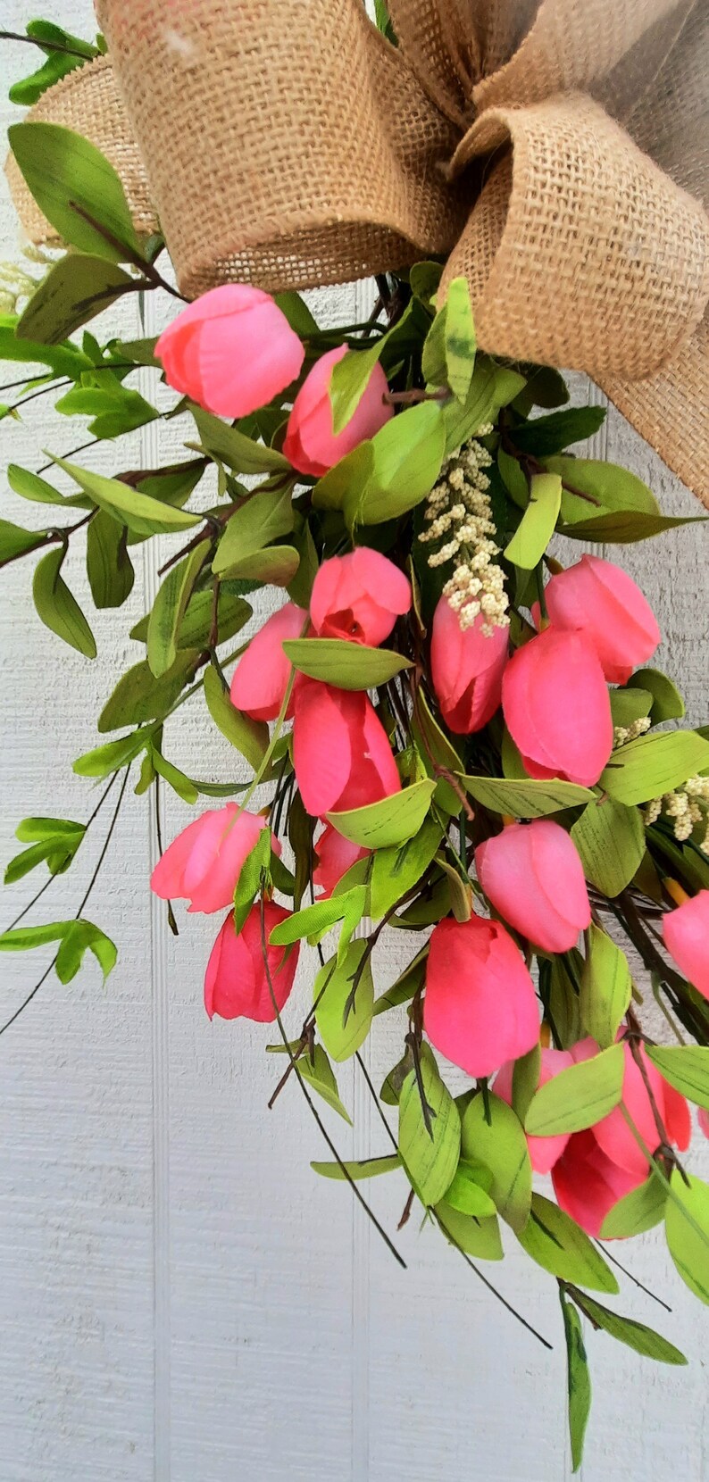 K&ouml;nnte beinhalten: Ein rosafarbener und gr&uuml;ner Blumenkranz mit einer Schleife aus Sackleinen. Der Kranz besteht aus k&uuml;nstlichen Blumen und Gr&uuml;n.