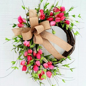 K&ouml;nnte beinhalten: Ein Kranz aus rosa Tulpen mit einer Schleife aus Sackleinen. Der Kranz ist aus Weinreben gefertigt und mit rosa Tulpen und Gr&uuml;n verziert.