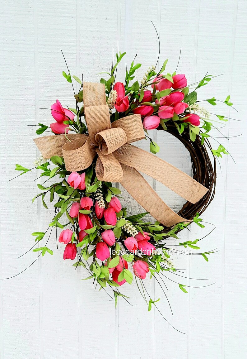 K&ouml;nnte beinhalten: Ein Kranz aus rosa Tulpen mit einer Schleife aus Sackleinen. Der Kranz ist aus Weinreben gefertigt und mit rosa Tulpen und Gr&uuml;n verziert.