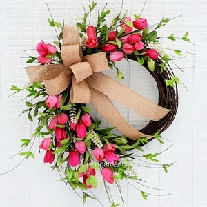 K&ouml;nnte beinhalten: Ein Fr&uuml;hlingskranz mit einer Schleife aus Sackleinen und rosa Tulpen. Der Kranz ist aus Weinreben gefertigt und mit gr&uuml;nen Bl&auml;ttern verziert.