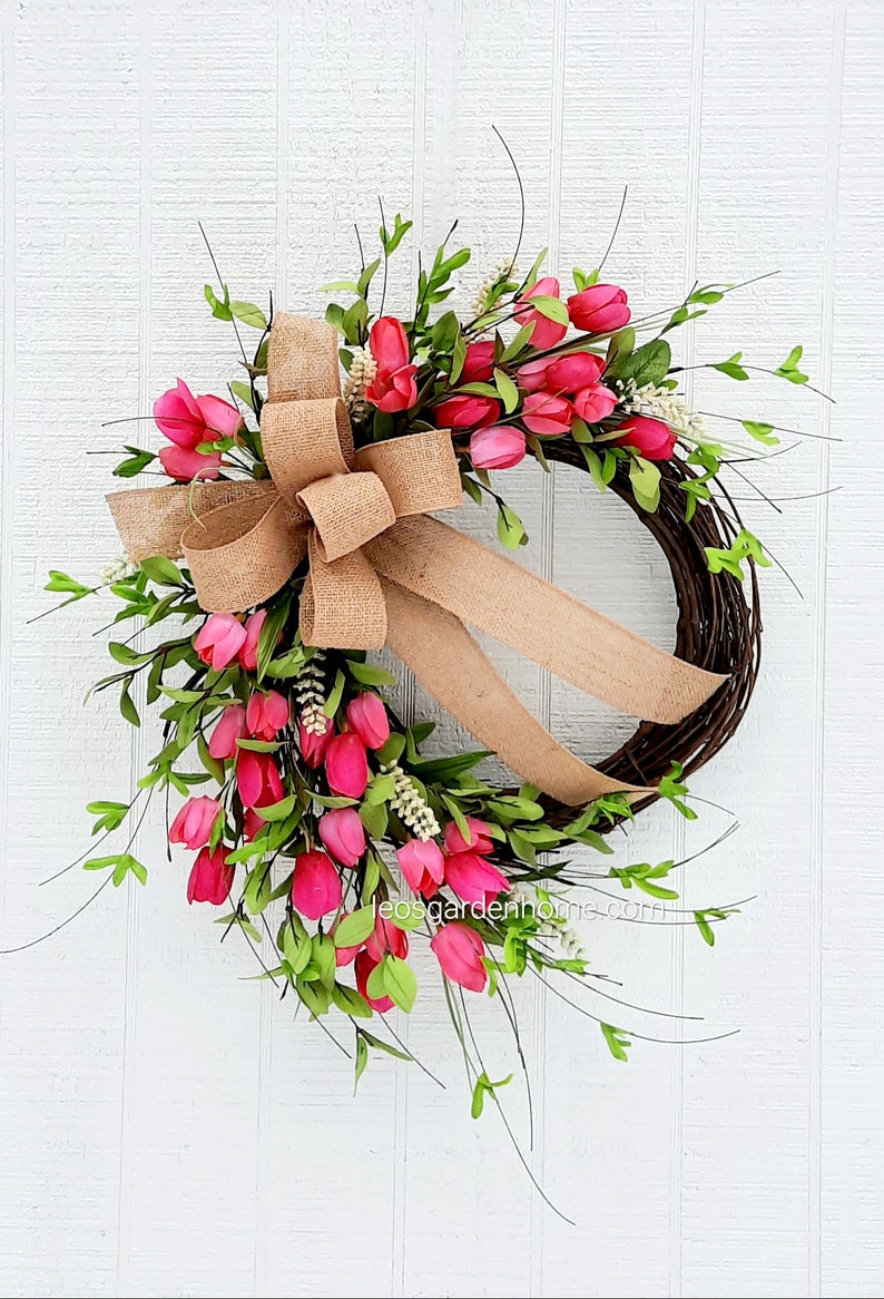 K&ouml;nnte beinhalten: Ein Fr&uuml;hlingskranz mit einer Schleife aus Sackleinen und rosa Tulpen. Der Kranz ist aus Weinreben gefertigt und mit gr&uuml;nen Bl&auml;ttern verziert.