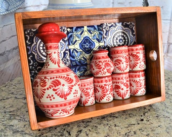 Puede incluir: Una bandeja de madera con un juego de cerámica Talavera roja y blanca, que incluye una jarra y vasos de chupito. La bandeja está decorada con azulejos mexicanos coloridos.