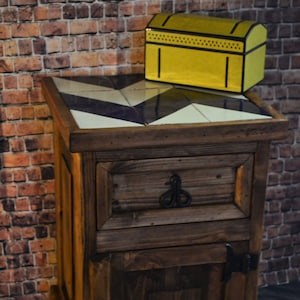 May include: A dark brown wooden bedside table with a single drawer and a cupboard door. The top of the bedside table is decorated with a black and white geometric tile pattern. A yellow box with black trim sits on top of the bedside table.