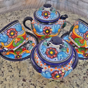 Puede incluir: Un juego de cerámica mexicana Talavera de colores incluye una tetera, un azucarero y dos tazas y platillos. La cerámica presenta un diseño floral azul, blanco, naranja y verde.