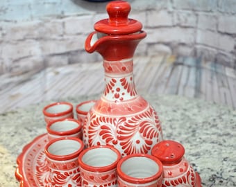 Puede incluir: Un juego de cerámica rojo y blanco para beber. El juego incluye una jarra con tapa, seis tazas pequeñas, un salero y una bandeja. Las piezas están decoradas con un estampado floral.