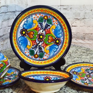 Puede incluir: Un juego de cerámica Talavera colorida incluye un tazón, un plato, una taza y un platillo. Los platos presentan un patrón floral azul, amarillo, naranja y verde.