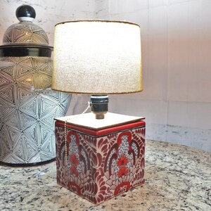 Puede incluir: Una lámpara de mesa de cerámica roja y blanca con un diseño floral. La lámpara tiene una pantalla de lino blanca y una cadena de tracción.