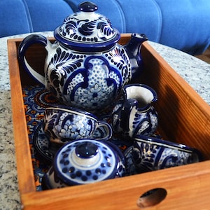 May include: A wooden tray containing a blue and white ceramic tea set. The set includes a teapot, creamer, and four cups. The tray has a handle and a round hole in the side.