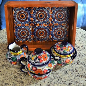May include: A wooden tray with a colourful tile design, featuring four ceramic bowls with floral patterns in shades of blue, yellow, orange, and green. The bowls have lids and are ideal for serving snacks or condiments.