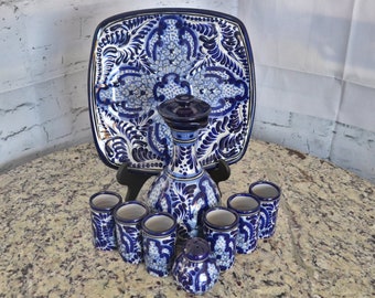 May include: A blue and white Talavera pottery set with a pitcher, six shot glasses, and a square serving tray. The set features intricate floral designs.