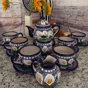 May include: A ceramic tea set featuring a dark blue and white hand-painted calla lily pattern. The set includes a teapot with a lid, a sugar bowl with a lid, a creamer, and several teacups with matching saucers, all decorated with intricate floral motifs.