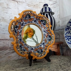May include: A yellow ceramic plate with a blue and white floral design and a round mirror in the center. The plate is on a black stand and a sunflower is reflected in the mirror.