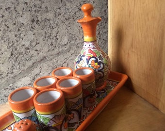 Puede incluir: Un juego de seis vasos de chupito de cerámica coloridos con una jarra a juego, todos decorados con motivos florales. El juego se muestra en una bandeja a juego.