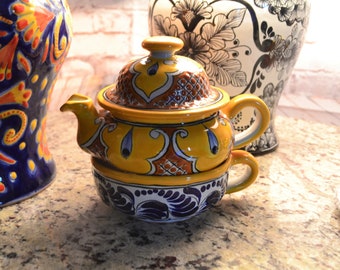 May include: A yellow ceramic teapot with a lid and a matching cup. The teapot and cup are decorated with blue and brown floral patterns.