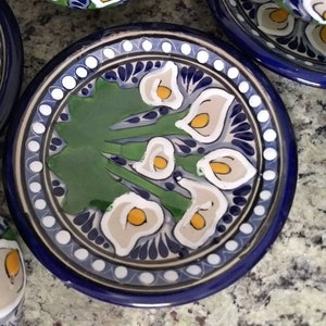 K&ouml;nnte beinhalten: Eine blaue und wei&szlig;e Keramik-Untertasse mit einem gr&uuml;nen, wei&szlig;en und gelben Blumendesign. Die Untertasse hat einen Rand aus wei&szlig;en Punkten und einen blauen Rand.