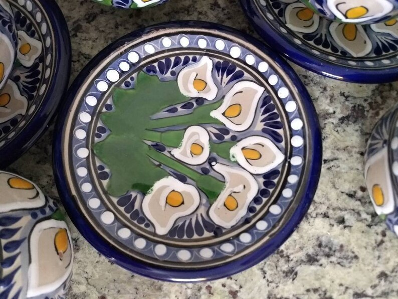 K&ouml;nnte beinhalten: Eine blaue und wei&szlig;e Keramik-Untertasse mit einem gr&uuml;nen, wei&szlig;en und gelben Blumendesign. Die Untertasse hat einen Rand aus wei&szlig;en Punkten und einen blauen Rand.