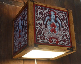 Puede incluir: Una lámpara de pared de madera con una baldosa cuadrada blanca con un diseño floral rojo, rosa y azul. La lámpara tiene una luz en el interior.