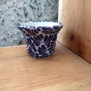 May include: A small white ceramic planter with a blue and white floral pattern. The planter is sitting on a wooden surface.
