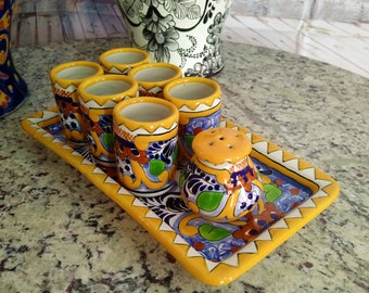 Puede incluir: Un juego de seis vasos de chupito de cerámica coloridos con una bandeja a juego y un pequeño salero. Los vasos y la bandeja están decorados con un patrón tradicional mexicano Talavera en tonos de azul, verde, amarillo y naranja.
