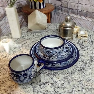 May include: Two blue and white ceramic mugs with floral designs, one with a handle, on a granite worktop with a blue and white ceramic saucer.