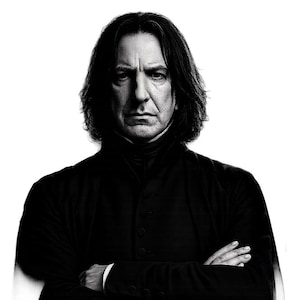 May include: Black and white portrait of a man with long, dark hair and a stern expression. He is wearing a dark, button-down coat with a high collar, arms crossed. The image is a studio shot with a white background.