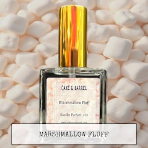 May include: A perfume bottle with a gold cap and a label that reads "Cake & Barrel Marshmallow Fluff Eau De Parfum 1 oz." The bottle is set against a background of white marshmallows, with the words "Marshmallow Fluff" in a white box below.