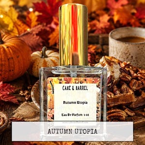 May include: A clear glass perfume bottle with a gold cap and a rectangular label featuring the text Cake & Barrel, Autumn Utopia, and Eau De Parfum 1 oz. The bottle is centered in the frame, showcasing a transparent liquid inside the container.