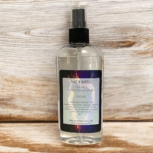 May include: A clear glass bottle with a black spray top. The bottle is labeled "Cake & Barrel Sea Salt Texturizing Spray Desire Shake Well Before Use Ingredients: Distilled Water, Vegan Cellulose, Sodium Chloride, Aloe Vera Juice, Coconut Oil, Chamomile Extract, Avocado Oil, Jojoba Oil, Monoi Tiare Oil, Caprylyl Glycol, Phenoxyethanol, Fragrance 4 fl oz www.cakeandbarrel.com Fort Oglethorpe, GA"