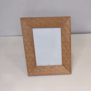 May include: A light brown wooden picture frame with a geometric pattern. The frame is standing upright on a white surface.