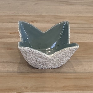 May include: A small, star-shaped ceramic bowl with a white textured exterior and a light blue interior.