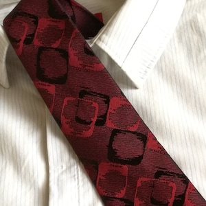 May include: A dark red tie with a geometric pattern of black and red squares. The tie is made of a silky fabric and has a classic design.