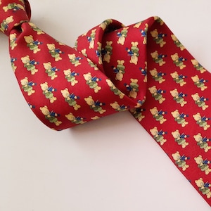 May include: A red silk tie with a repeating pattern of yellow teddy bears playing musical instruments.