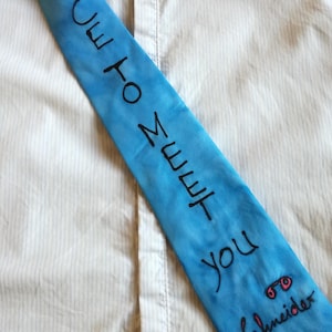 Può includere: Una cravatta blu con il testo "I'll to meet you" e un disegno di occhiali con il testo "Schneider" sotto.