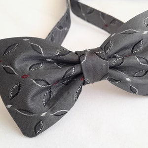 Può includere: Un papillon grigio con un motivo a foglie bianche e rosse.