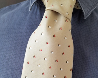 May include: A beige silk tie with a pattern of small white, red, and brown shapes. The tie is tied in a knot and is worn against a blue shirt.