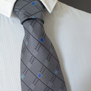 May include: A gray patterned tie with blue and white accents. The tie has a diagonal pattern of stripes and squares.