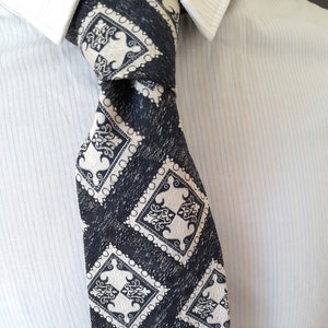 May include: A black and white patterned tie with a geometric design. The tie is made of a textured fabric and has a subtle sheen.