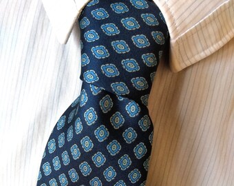 Puede incluir: Una corbata de patrón azul y blanco con un diseño geométrico. La corbata está anudada y se usa con una camisa blanca.